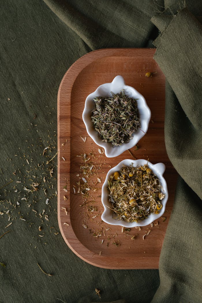 Dried chamomile and herbs in white bowls on a wooden tray, perfect for herbal tea themes.